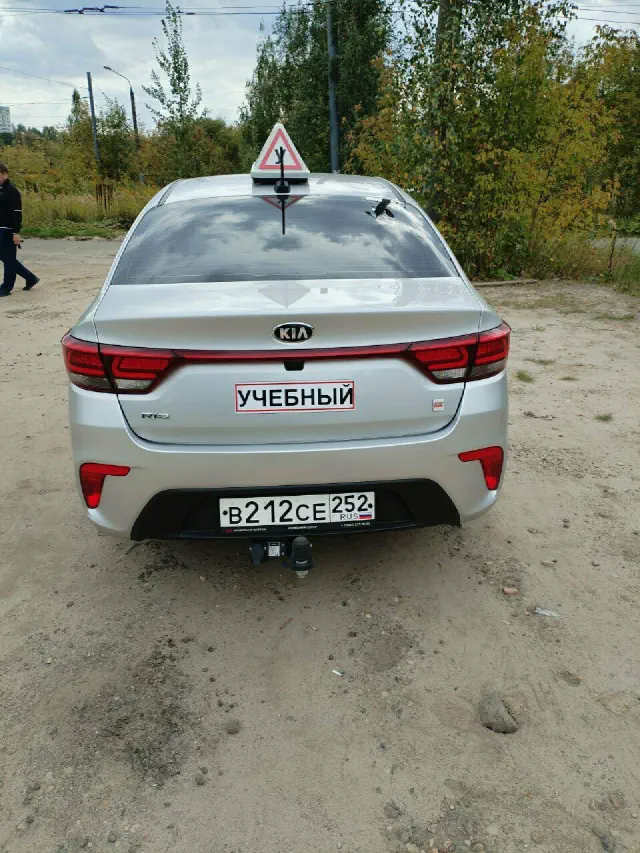 Серебристый учебный Kia Rio с надписью «Учебный», вид сзади
